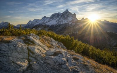 Photo of sunrise peeking over jagged mountains.