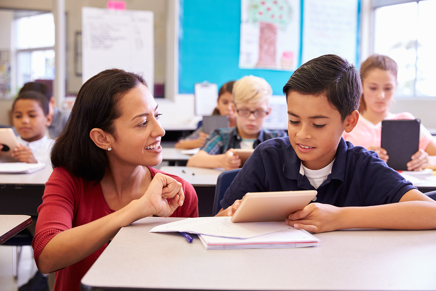 Teacher helping elementary school boy using tablet computer