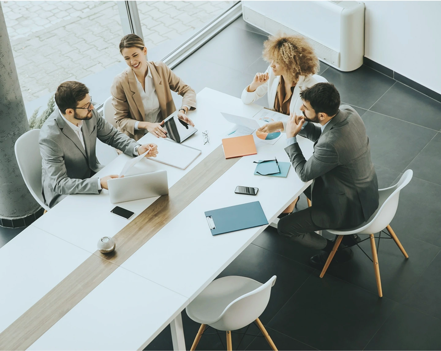 Two women and two men, professionals, sitting around a conference table talking, laptop and papers spread about.